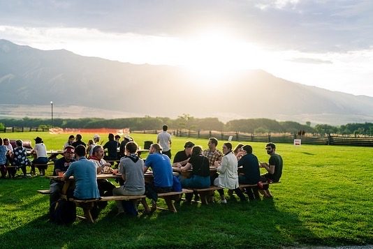 Long dinner tables on a lawn at sunset with mountains in the distance