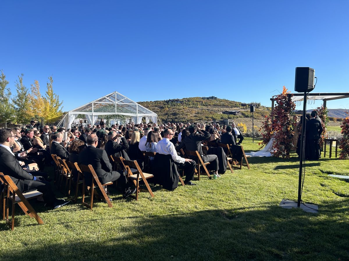 Outdoor ceremony sound with a discreet speaker on a stand under a clear-top tent and mountain backdrop